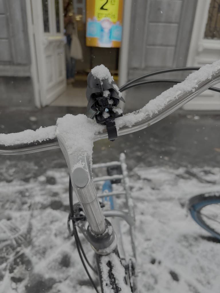 Black BajkBuddy figurine attached to a snowy bike handlebar