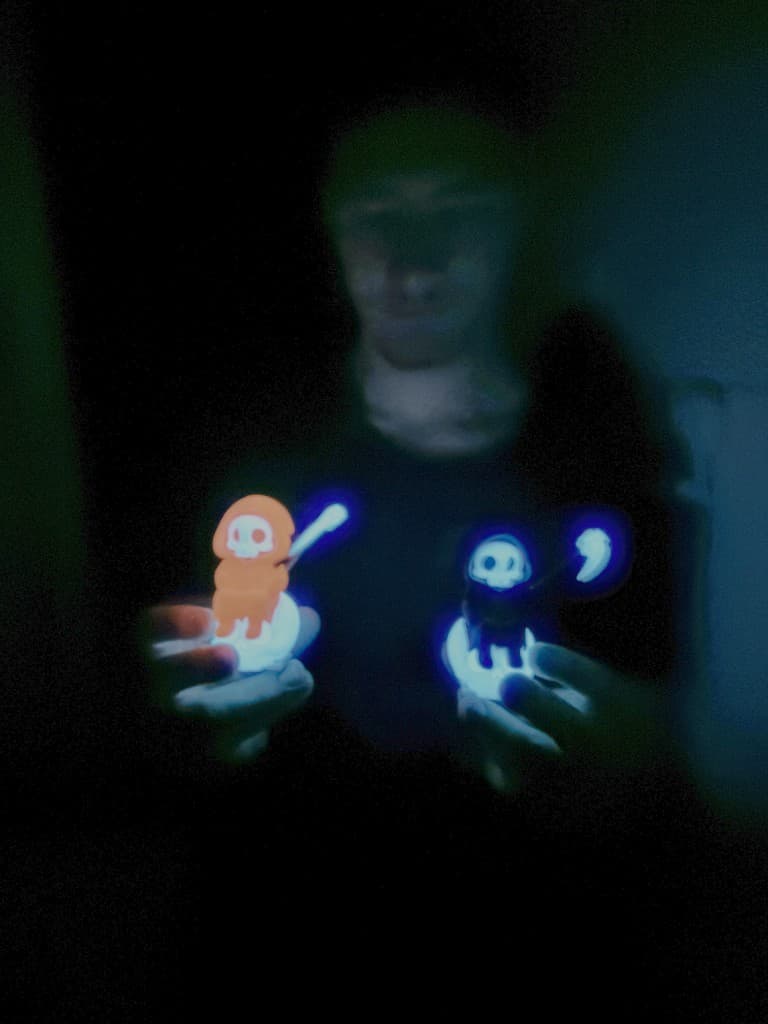 Two glowing BajkBuddy figurines held in the dark